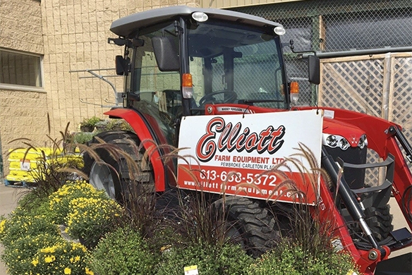 Red Massey Ferguson tractor parked in front of Elliott Farm Equipment, surrounded by fall flowers and dealership signage.
